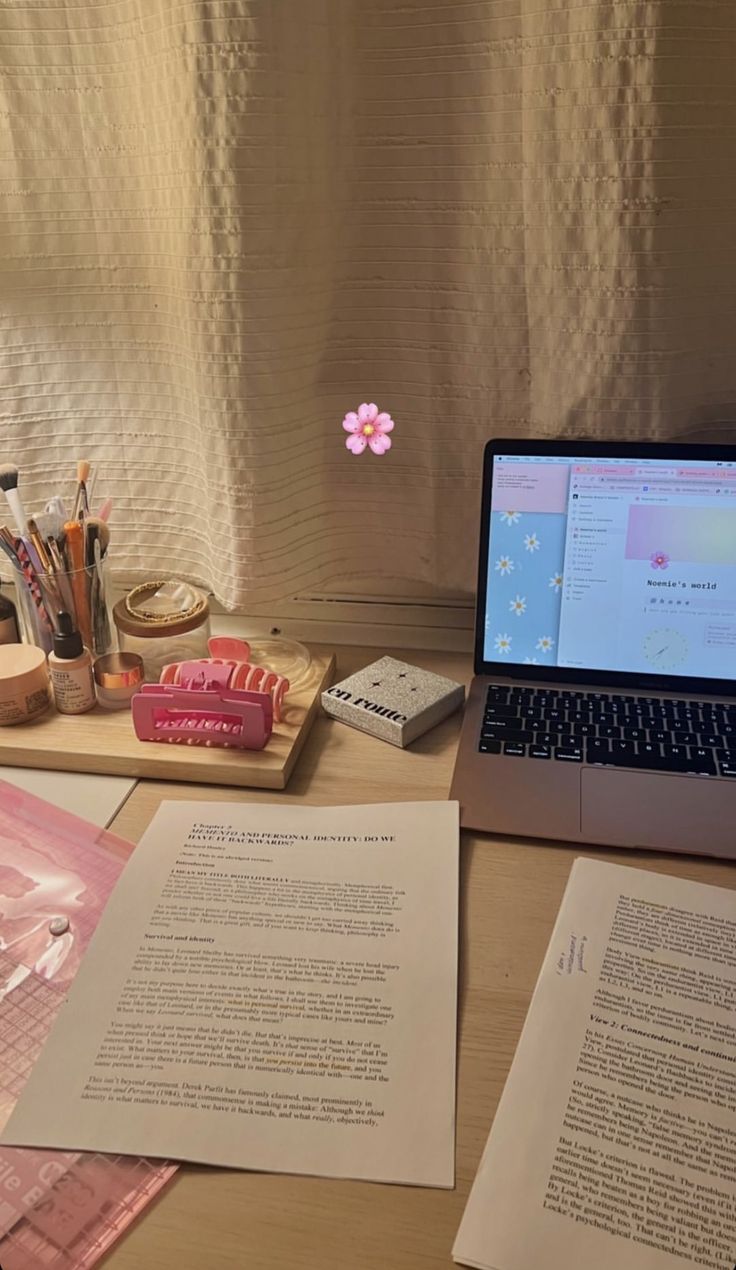 an open laptop computer sitting on top of a wooden desk next to papers and pens