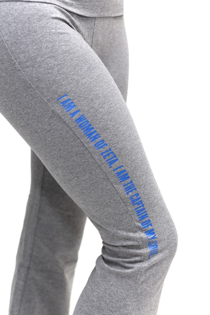 a woman in grey sweat pants with blue writing on the leggings and her hands behind her back