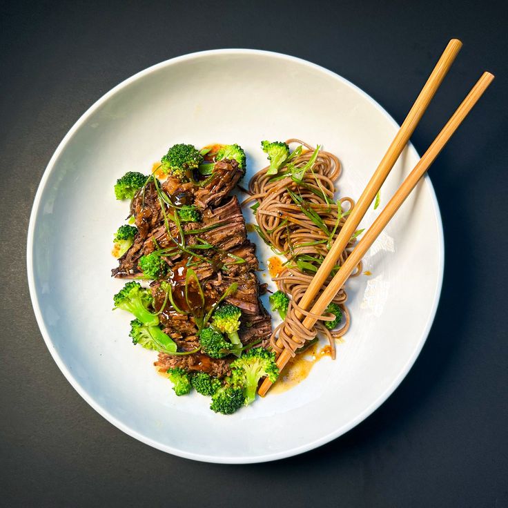 a white plate topped with beef and broccoli covered in sauce next to chopsticks