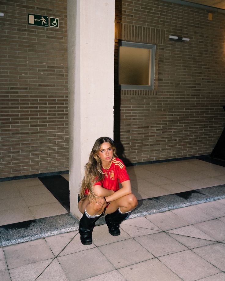 a woman sitting on the ground in front of a building with her legs crossed and wearing knee high boots