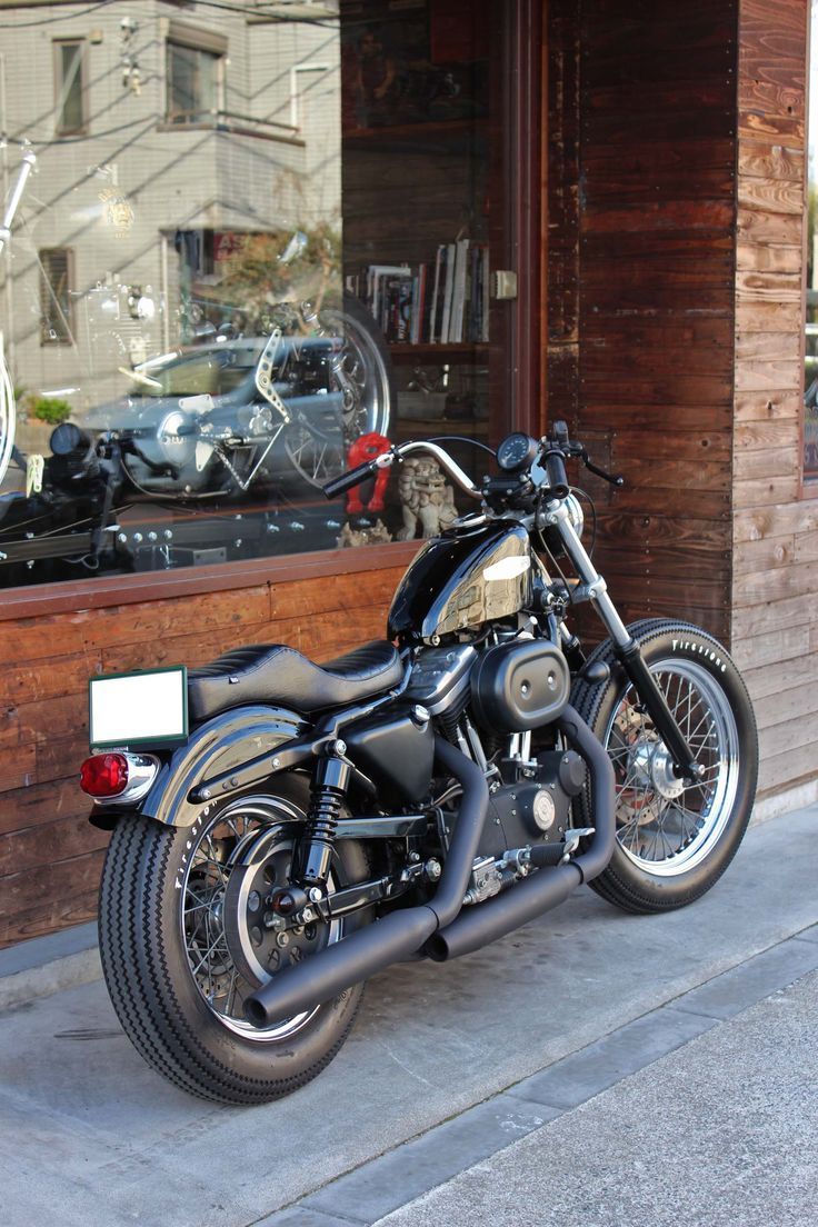 a black motorcycle parked in front of a store window with the reflection of another bike behind it