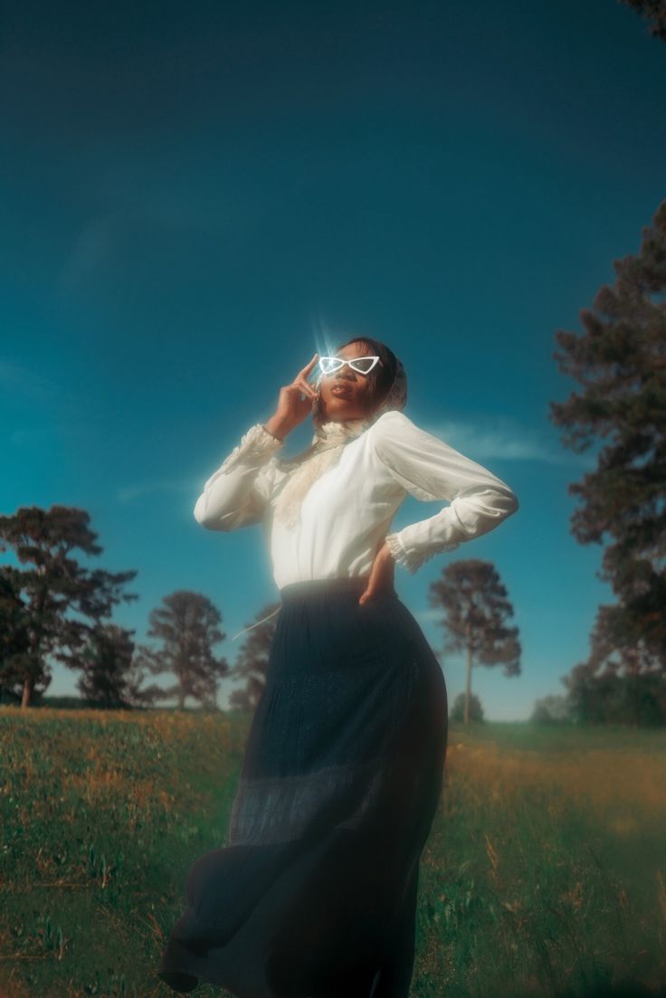 a woman standing in a field with her hands on her head and looking up at the sky