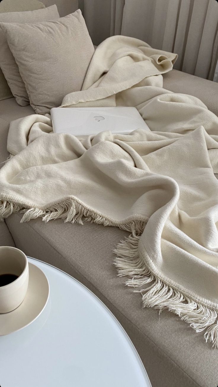 an open laptop computer sitting on top of a couch next to pillows and a cup