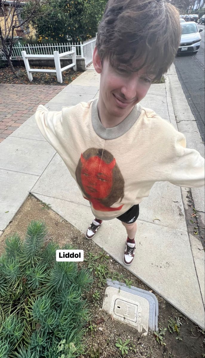 a young boy standing on top of a sidewalk next to a green plant filled with dirt