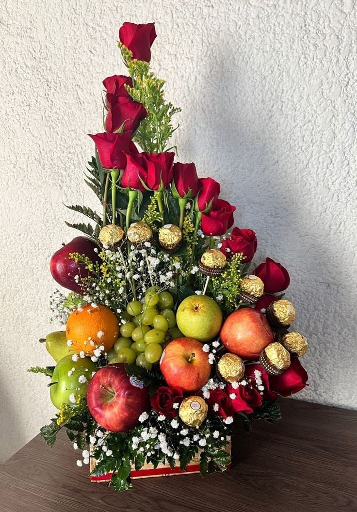 a basket filled with lots of fruit and flowers on top of a wooden table next to a white wall