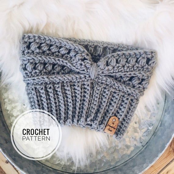 a gray knitted headband with a wooden button on the side sitting on top of a metal bowl