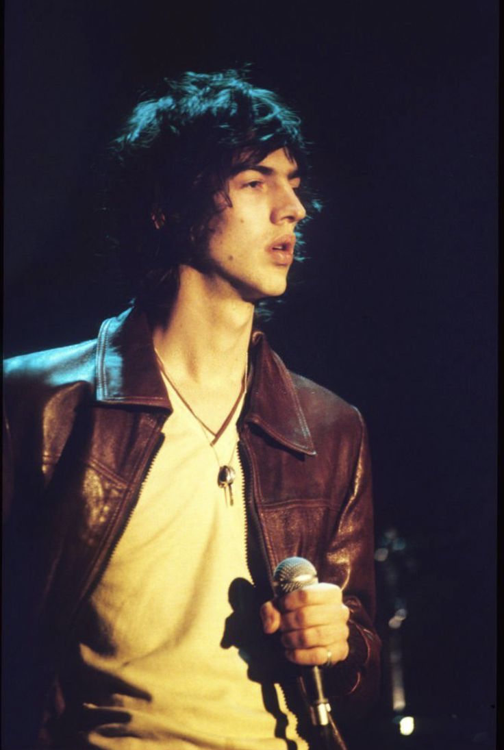 a man holding a microphone in his right hand and wearing a brown leather jacket on stage