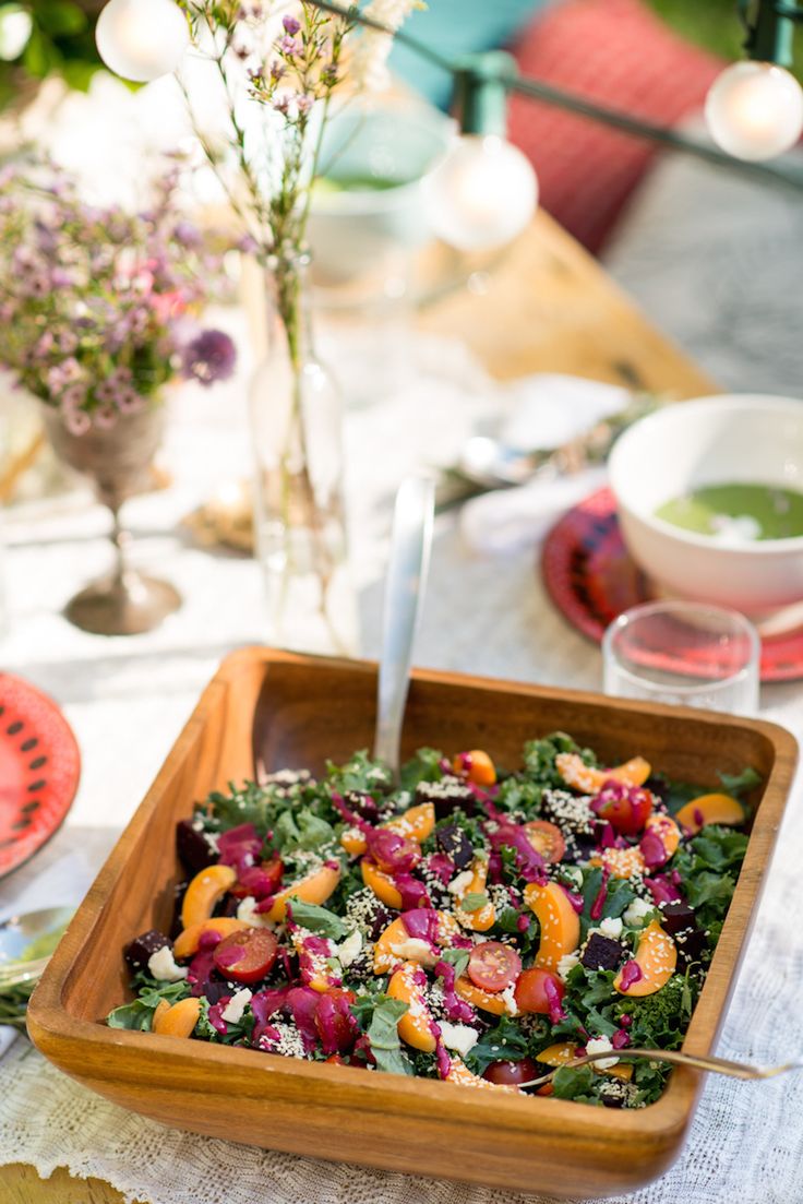 a wooden bowl filled with salad sitting on top of a white table covered in plates and utensils