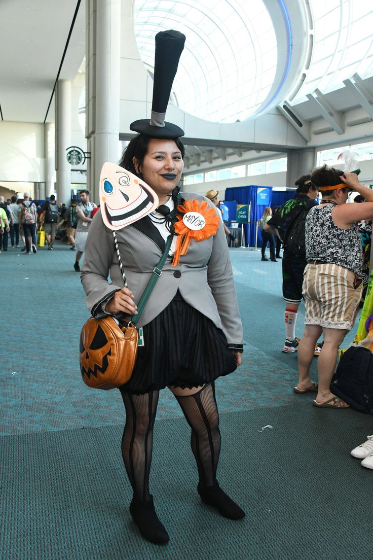 a woman dressed in costume and holding a jack - o'- lantern, standing inside an airport