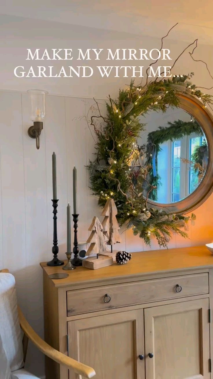 a mirror sitting on top of a wooden cabinet next to a table with candles and christmas decorations