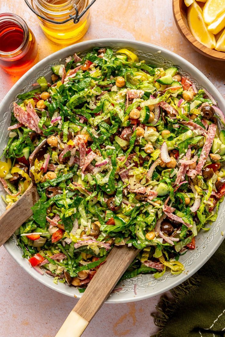 a salad with meat and vegetables in a bowl next to lemons, olives, and ketchup