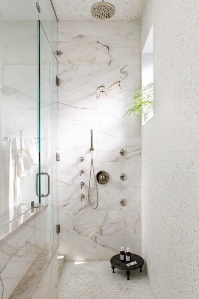 a walk in shower sitting next to a white tiled wall and counter top under a window