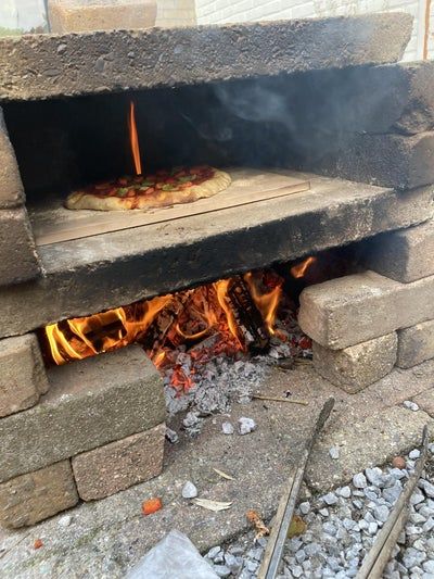 a pizza is cooking in an outdoor brick oven with flames coming out from the bottom