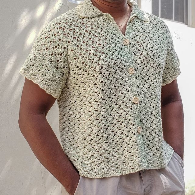 a man standing in front of a white wall wearing a crocheted shirt