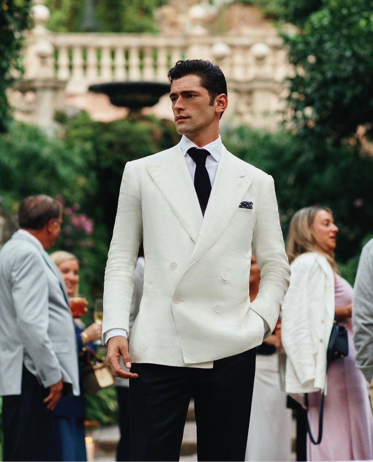 a man in a white suit and tie standing next to other people wearing formal wear