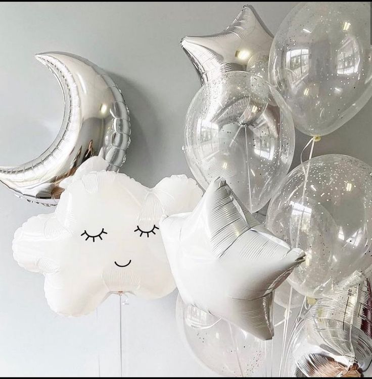 white balloons with silver foil stars and moon faces on them are hanging from the wall