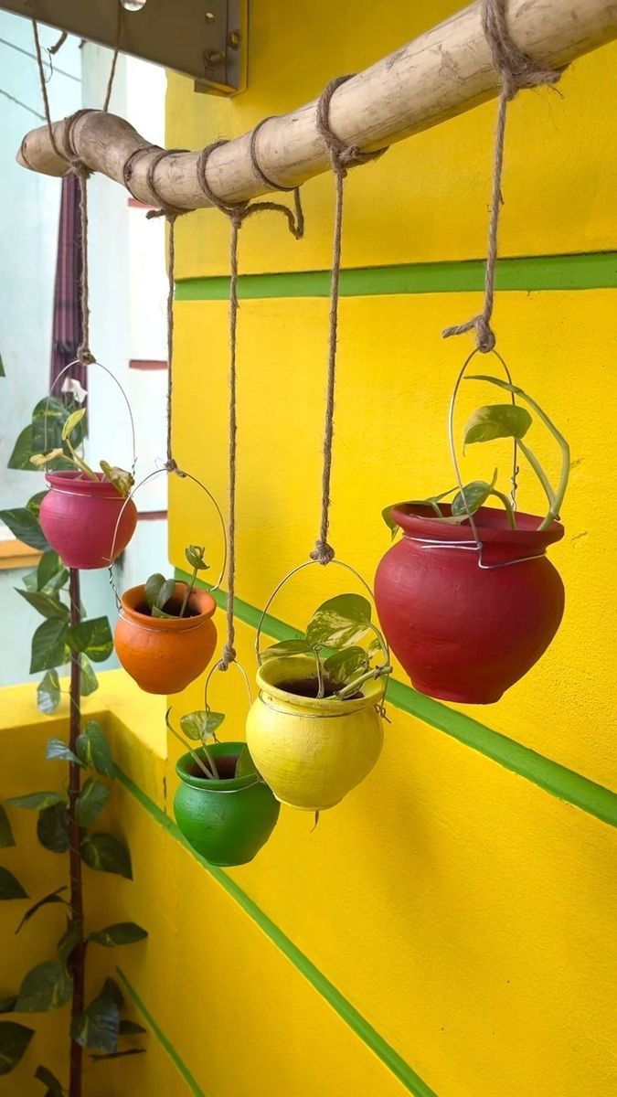 four hanging planters filled with plants on a yellow wall