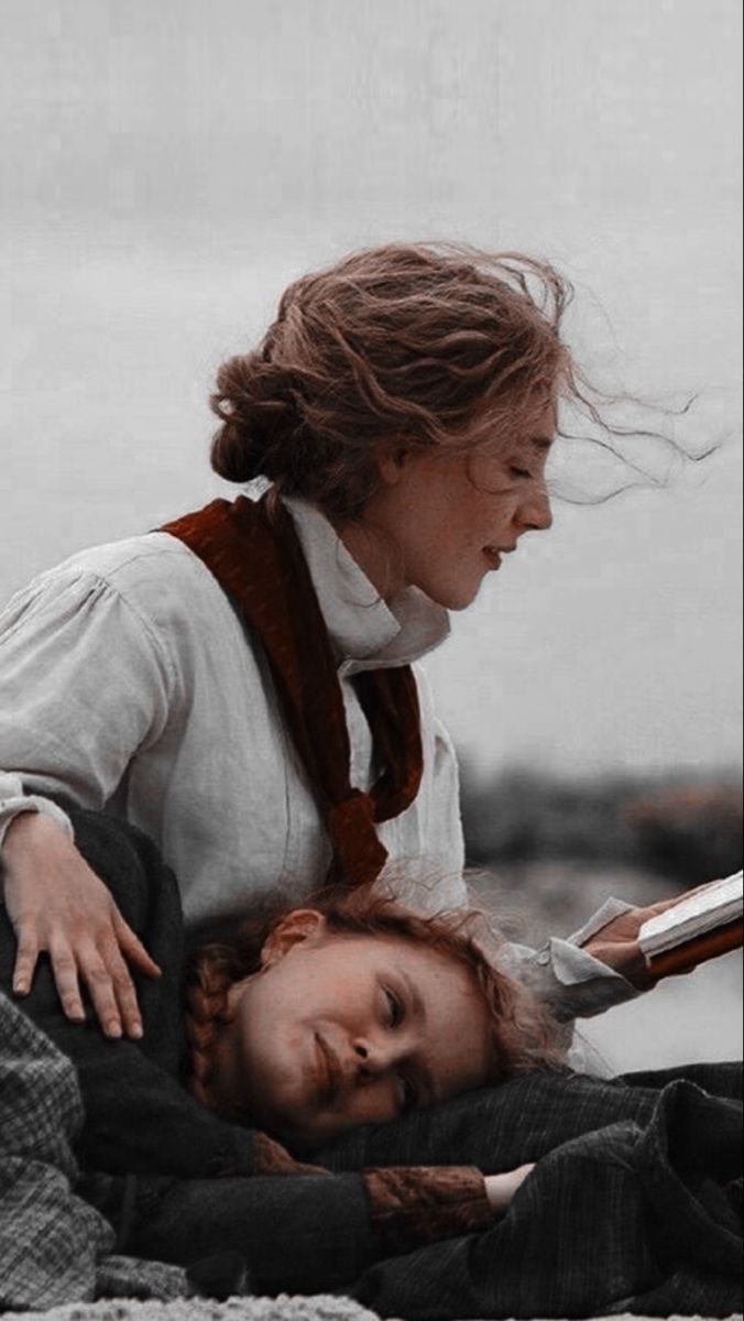 a woman reading a book to a child laying on the ground