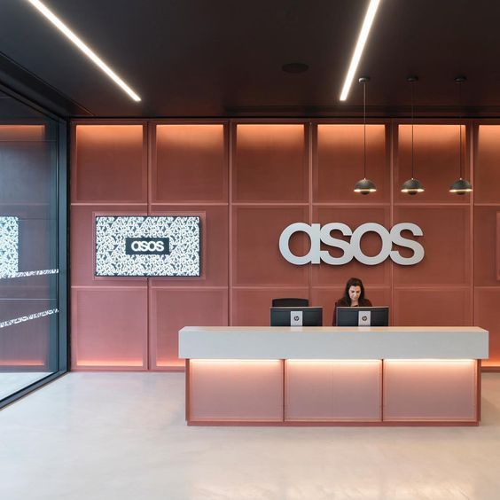 a woman sitting at a desk in front of a sign that says asos on it