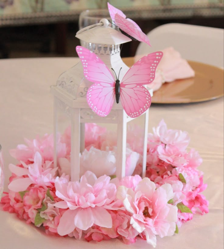 a table with pink flowers and a lantern on top of it that has butterflies flying out of it