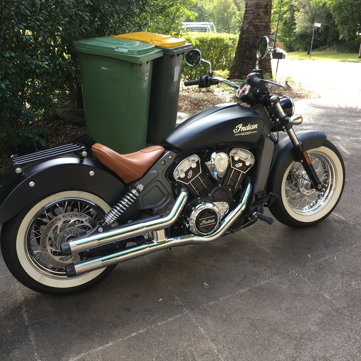 a black motorcycle parked next to a green trash can