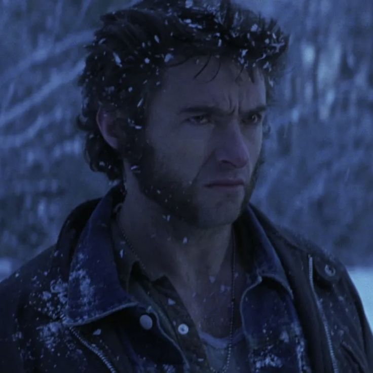 a man standing in the snow wearing a jacket and looking off into the distance with trees behind him