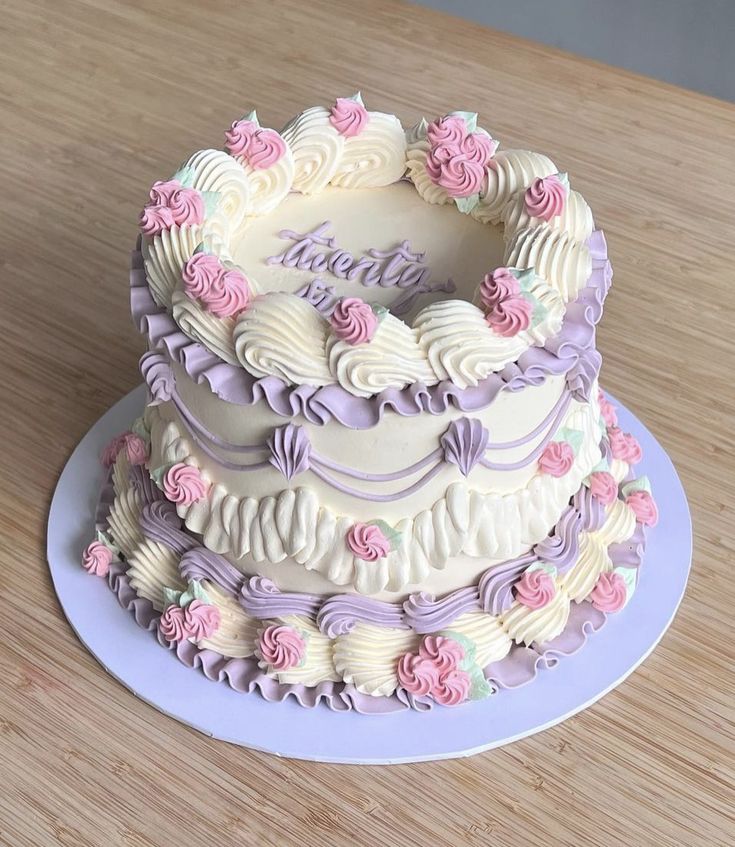 a three tiered cake with pink and purple frosting on a wooden table top