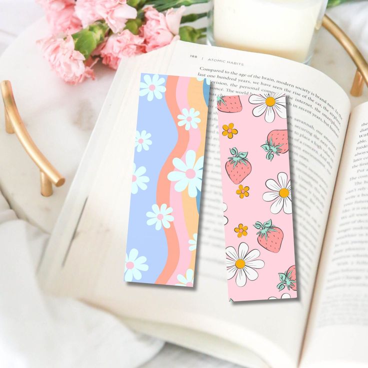 two bookmarks with strawberries and daisies on them are next to an open book