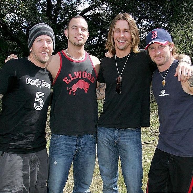 three men standing next to each other in front of trees and grass with one holding his arm around another man's shoulder