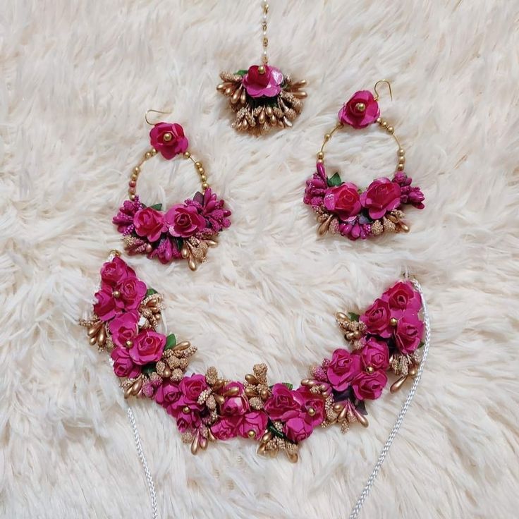 a necklace and earring set with pink flowers on white furnishing next to a pair of earrings