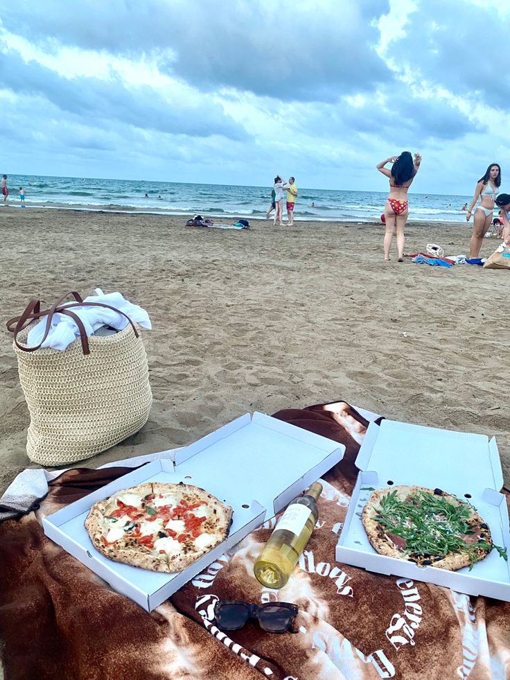 two pizzas are sitting on a blanket at the beach