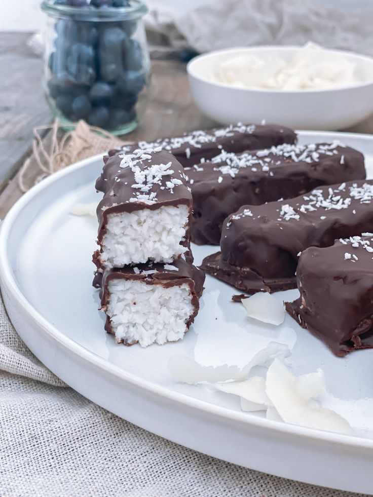 chocolate covered desserts sit on a plate with coconut flakes and powdered sugar