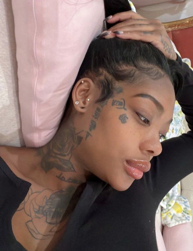 a woman with tattoos on her face and chest sitting in front of a pink pillow