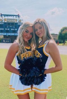 two cheerleaders posing for the camera in front of a stadium