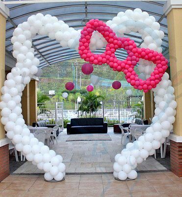 an arch decorated with balloons in the shape of a heart and pink bow on it