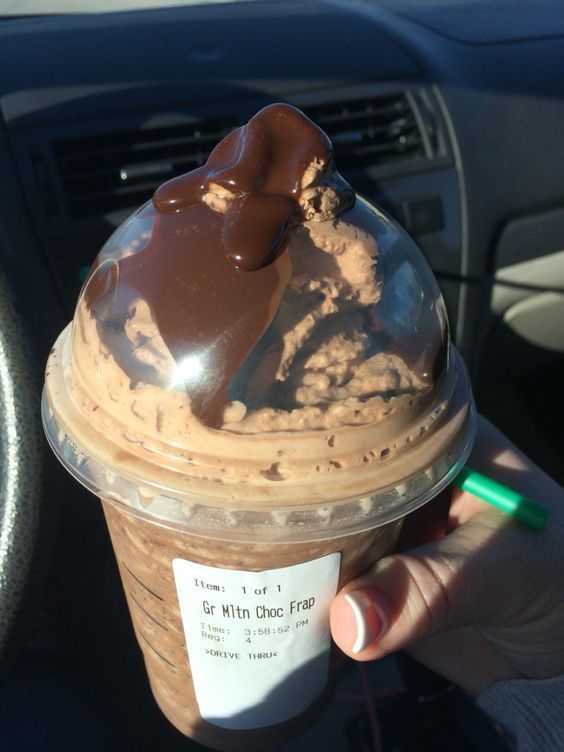 a person holding up a cup of ice cream with chocolate toppings on top in their hand