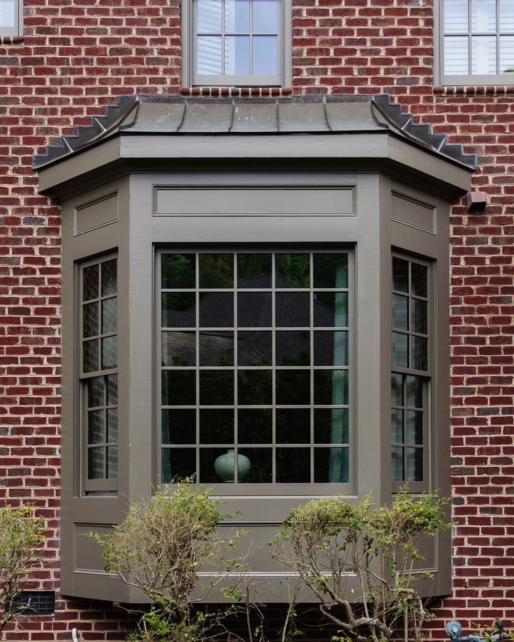 a window on the side of a brick building with plants growing in front of it