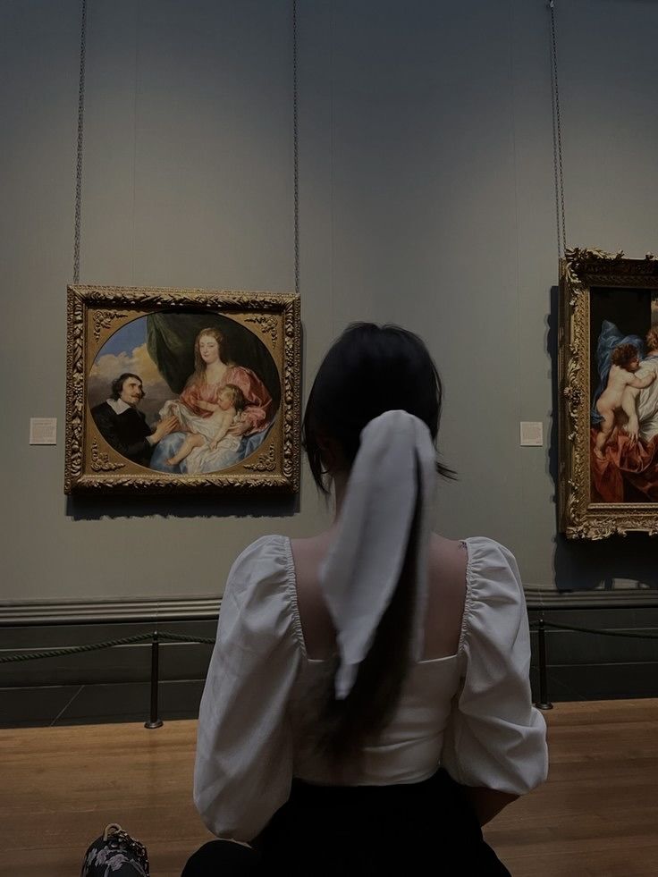 a woman sitting on the floor in front of two paintings with their backs turned to the camera