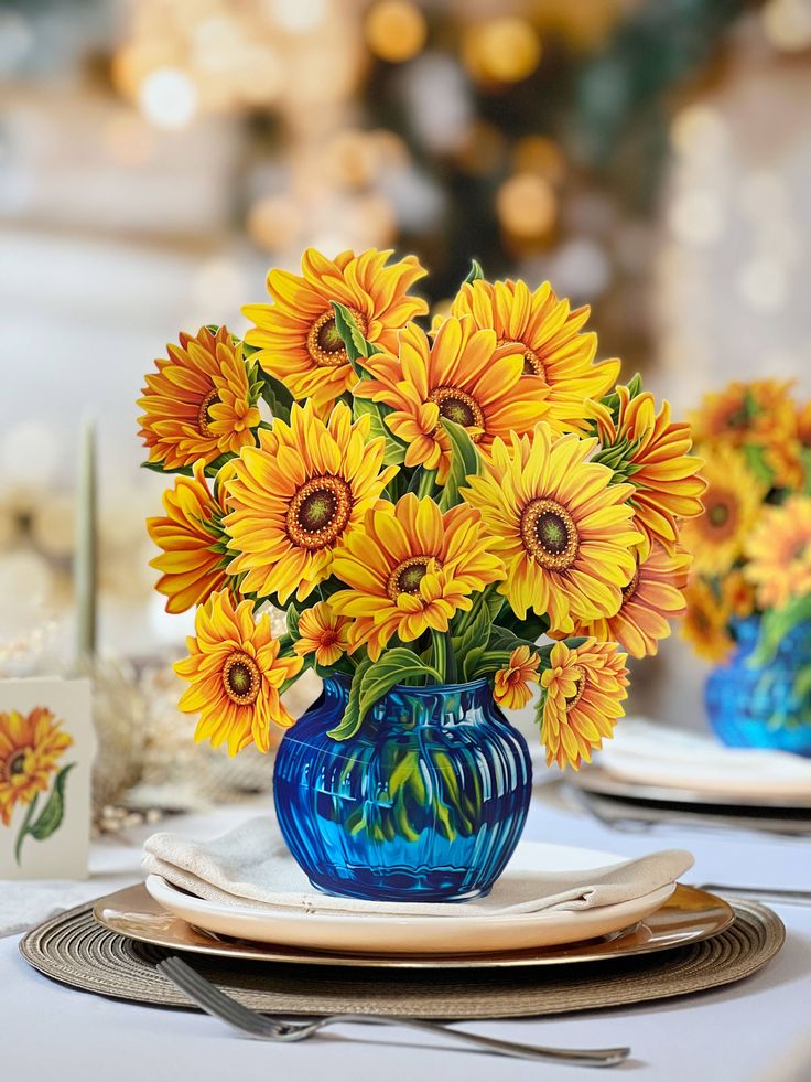 a blue vase filled with yellow sunflowers on top of a white table cloth