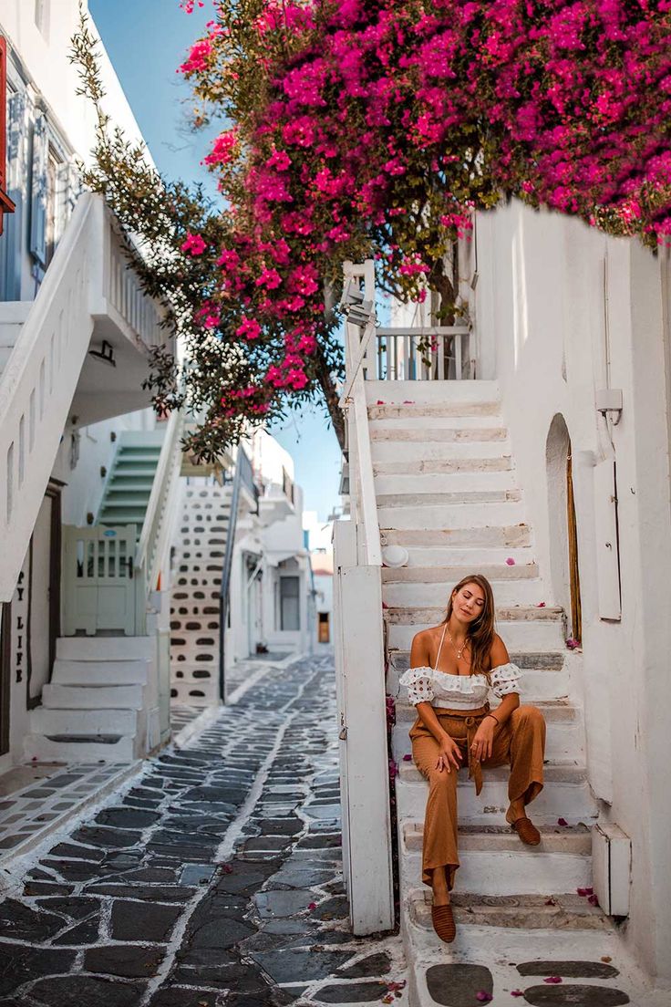 a woman is sitting on the steps in front of some pink bougaia trees