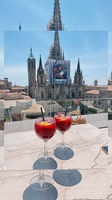 two wine glasses sitting on top of a table with red liquid in front of a castle