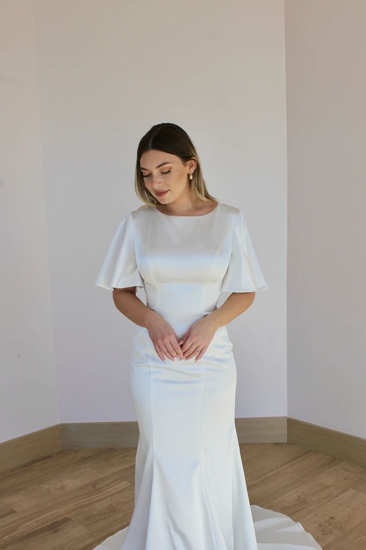 a woman in a white dress standing on a wooden floor with her hands behind her back