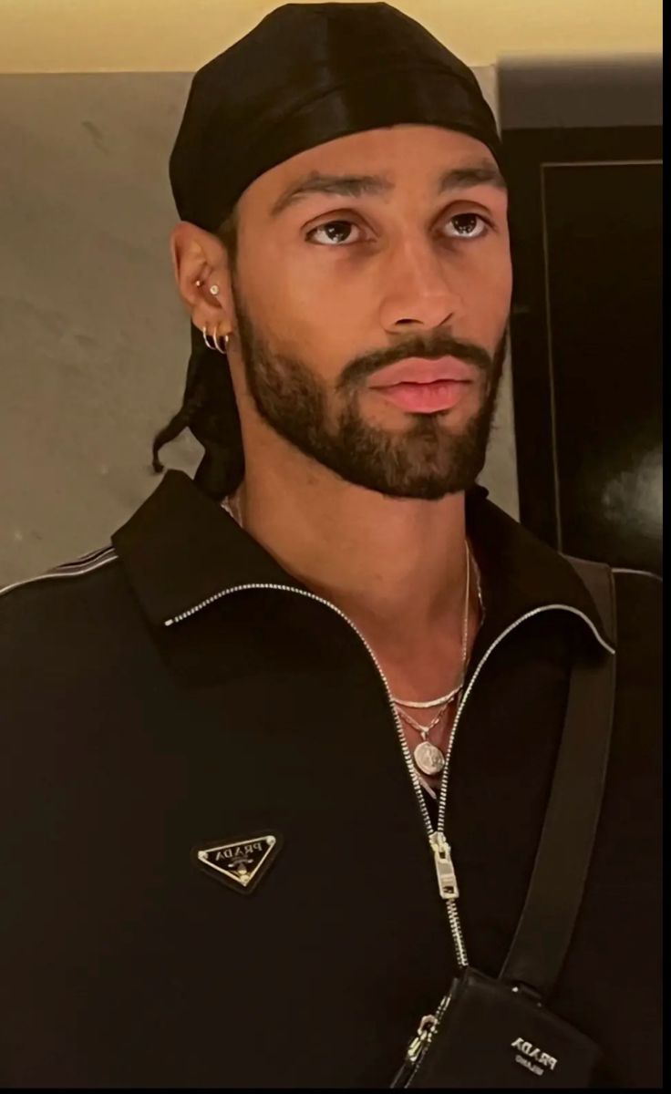 a man with a beard wearing a black jacket and silver chain around his neck is looking at the camera