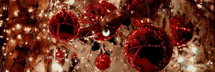 red ornaments hanging from a tree with lights around them