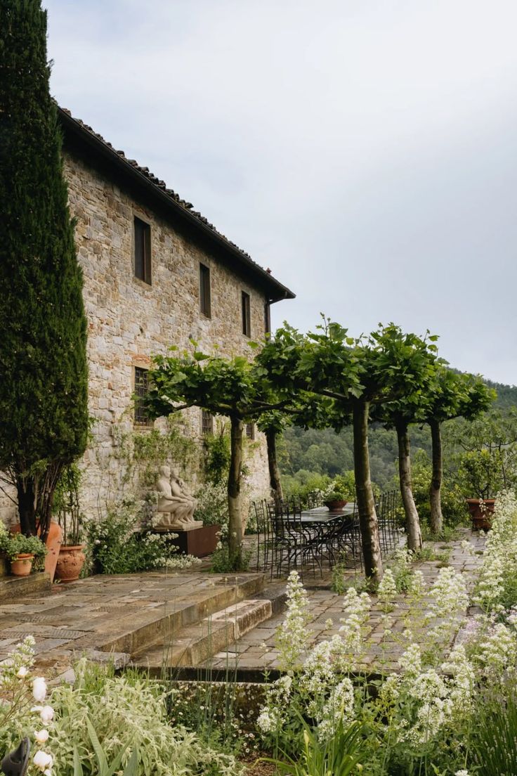 an outdoor patio with potted plants and chairs in the foreground, next to a stone building