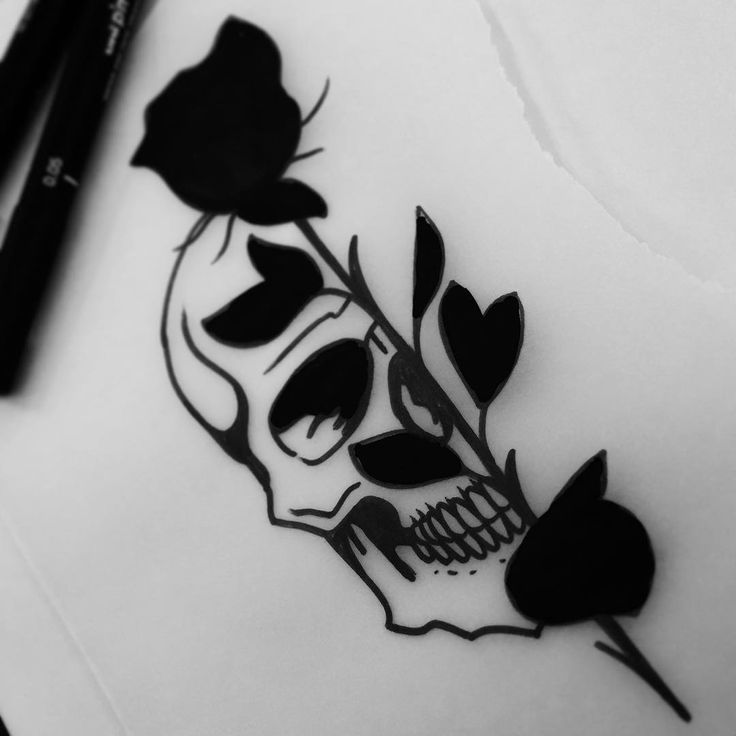 a black and white photo of a skull with flowers on it's head, next to two markers