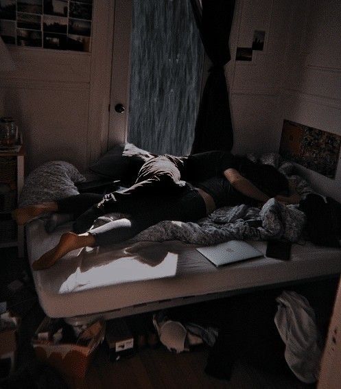 a woman laying on top of a bed in a room with lots of clutter