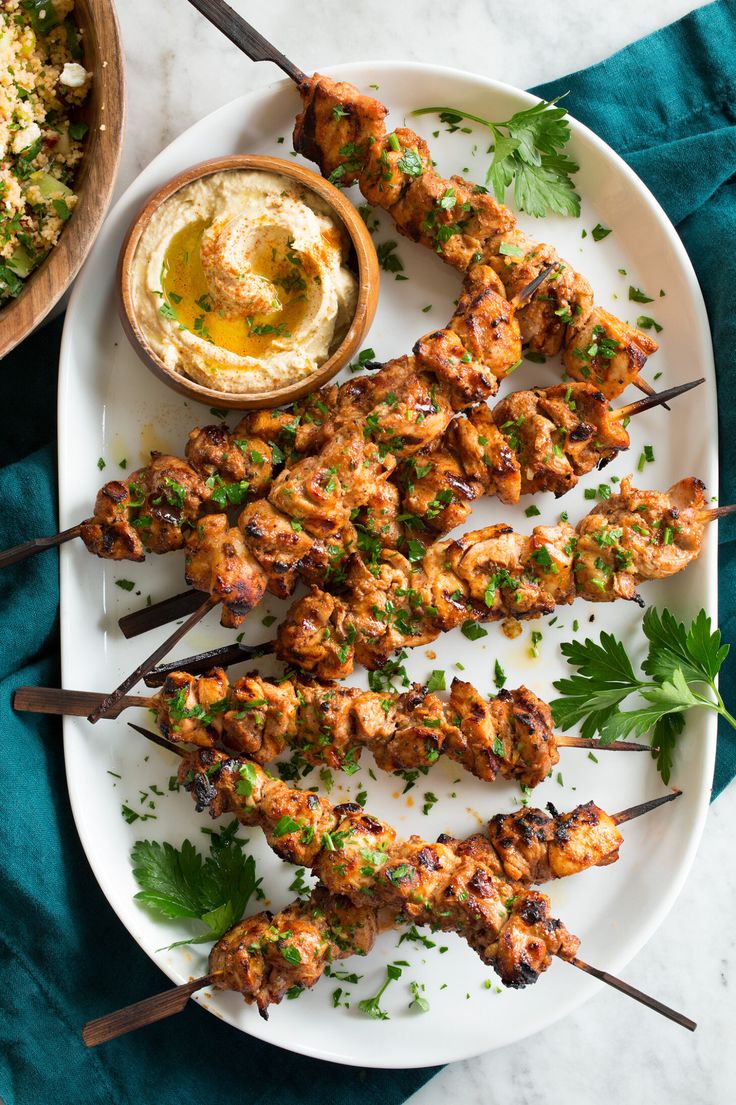 grilled chicken skewers on a white plate next to a bowl of dip