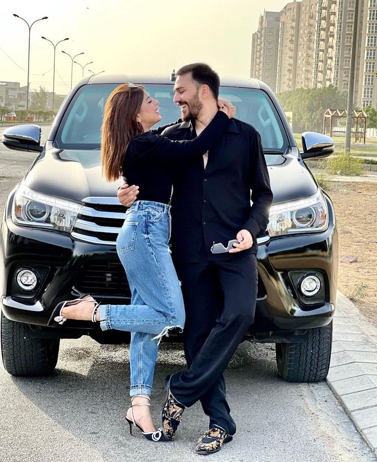 a man and woman standing next to a parked car with their arms around each other