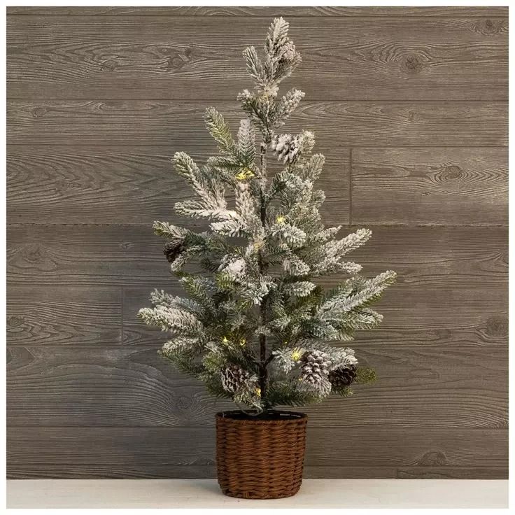 a small white christmas tree in a wicker basket with pine cones and lights on it